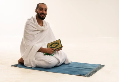 Saudi Pilgrim in Ihram Holding Quran on Prayer Mat