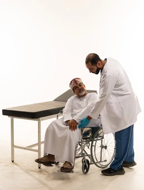طبيب عماني يساعد مريضاً مسناً على كرسي متحرك