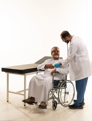 طبيب يفحص رجل عماني مسن على كرسي متحرك