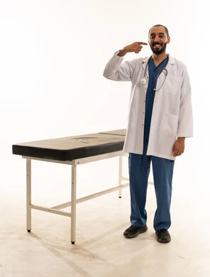 طبيب سعودي يشير إلى ابتسامته بجانب سرير الفحص الطبي