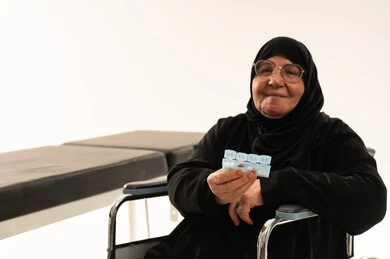 امرأة سعودية مسنة على كرسي متحرك مع منظم أدوية