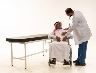 طبيب سعودي يفحص مريض مسن على كرسي متحرك