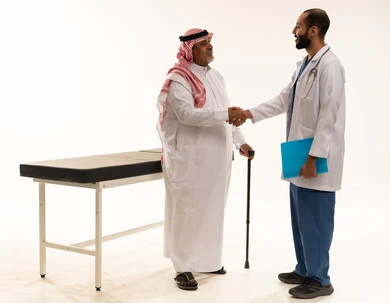 طبيب سعودي يصافح مريضاً مسناً في العيادة