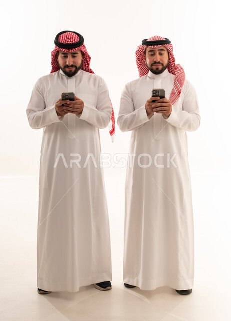 رجال سعوديون بالزي التقليدي يستخدمون الهواتف الذكية