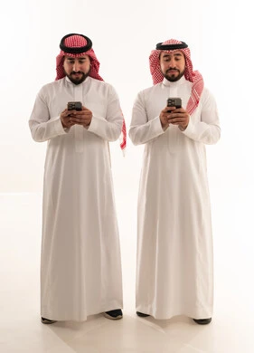 رجال سعوديون بالزي التقليدي يستخدمون الهواتف الذكية