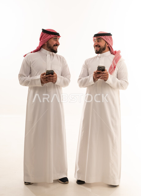 رجال سعوديون بالزي التقليدي يحملون هواتف ذكية بخلفية بيضاء