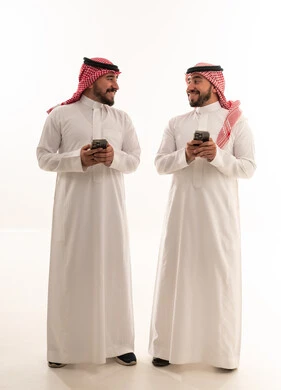 رجال سعوديون بالزي التقليدي يحملون هواتف ذكية بخلفية بيضاء