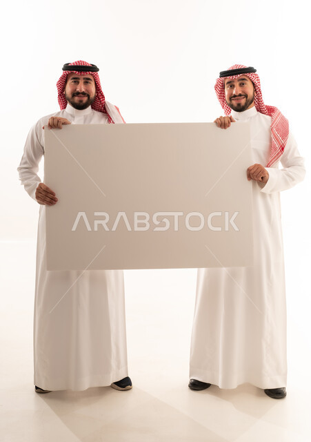 رجلان سعوديان يحملان لوحة بيضاء فارغة في استوديو