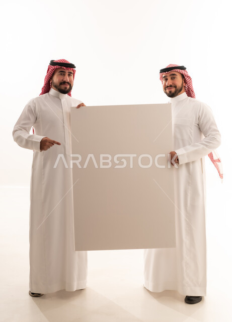 رجال سعوديون يحملون لوحة إعلانية بيضاء فارغة في الاستوديو