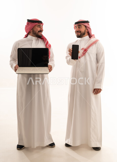 رجال سعوديون يحملون لابتوب وهاتف ذكي بخلفية بيضاء
