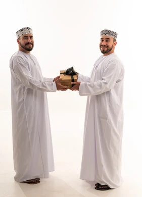 رجال عمانيون بالزي التقليدي يتبادلون الهدايا بخلفية بيضاء