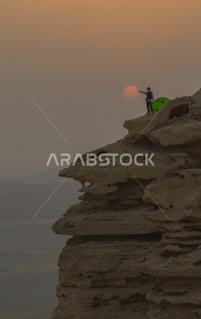 سائح عربي يقف في منطقة مطل نهاية العالم السياحة في الرياض وقت الغروب ، اماكن سياحية تاريخية بالمملكة العربية السعودية ، جبال طويق بنجد وقت الغروب ، حافة العالم في مدينة الرياض