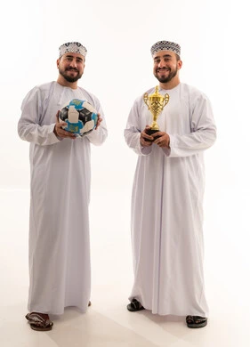 رجال عمانيون يحملون كأس البطولة وكرة قدم بخلفية بيضاء