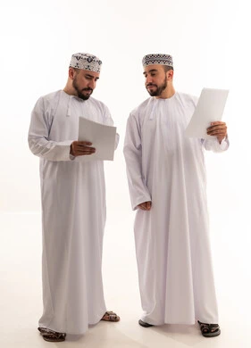 رجال عمانيون بالزي التقليدي يراجعون وثائق عمل
