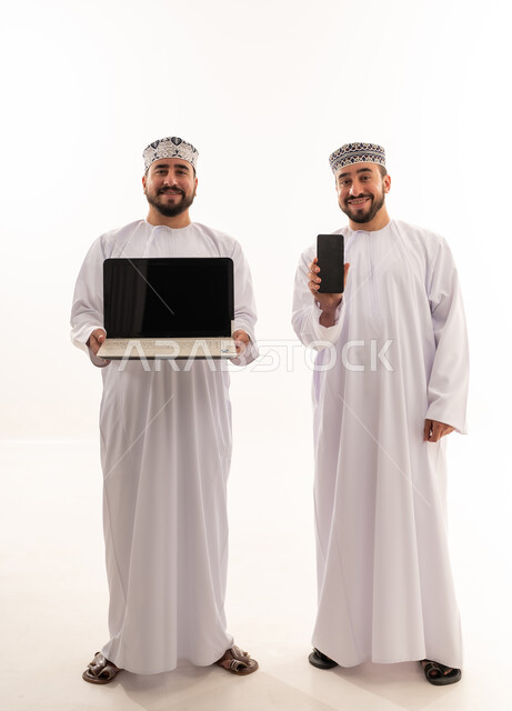رجال عمانيون يحملون لابتوب وهاتف ذكي في استوديو