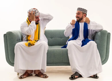 رجال عمانيون يتفاعلون مع مباراة كرة قدم على أريكة