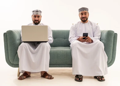 رجال عمانيون مع كمبيوتر وهاتف ذكي على أريكة