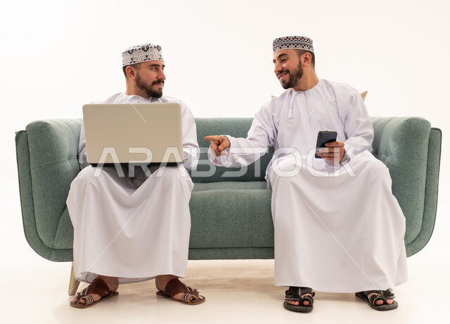 Omani Men Using Laptop and Smartphone on Sofa