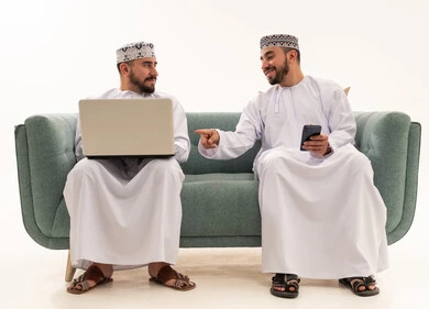 رجال عمانيون يستخدمون الحاسوب والهاتف على الأريكة