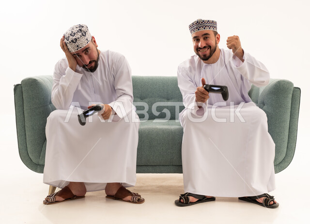 Omani Men Gaming on Sofa with Game Controllers