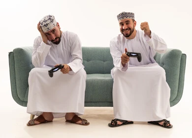 Omani Men Gaming on Sofa with Game Controllers