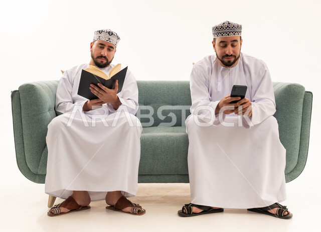 رجال عمانيون يقرؤون كتاباً ويستخدمون الجوال على الأريكة