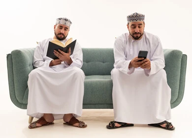 Omani Men Reading Book and Using Smartphone on Sofa