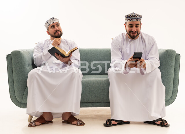 رجال عمانيون بالزي التقليدي مع كتاب وهاتف ذكي