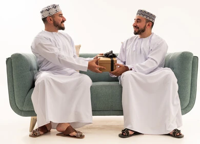 Omani Men in Traditional Dress Giving Gift on Sofa