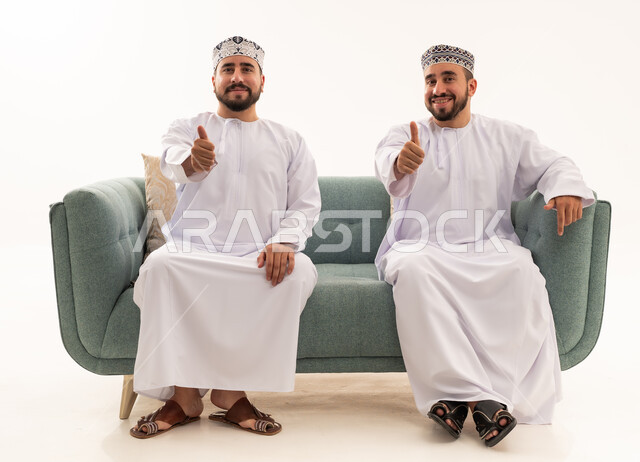 رجال عمانيون بإيماءة الإبهام للأعلى على الأريكة