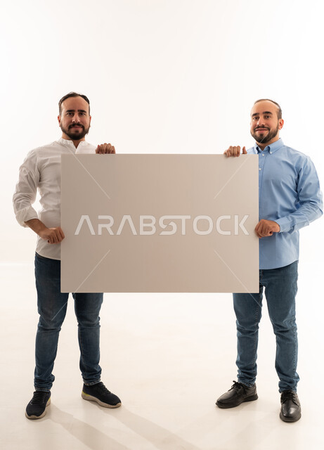 رجلان سعوديان يحملان لوحة بيضاء فارغة في استوديو