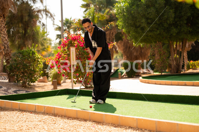 شاب سعودي يلعب الميني غولف في حديقة خارجية