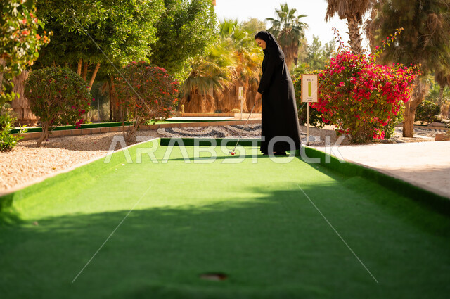 امرأة سعودية بالعباءة تلعب الغولف المصغر بالخارج