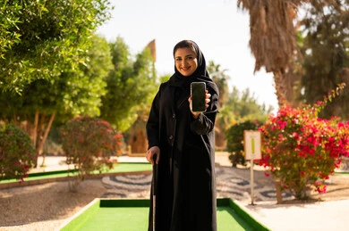 امرأة سعودية بالعباءة تحمل هاتف ذكي في ملعب جولف
