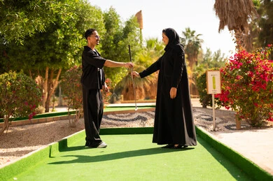 زوجين سعوديين يلعبان الجولف في حديقة خارجية مشمسة