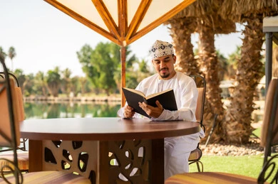 Omani Man in Traditional Dress Reading Book Outdoors