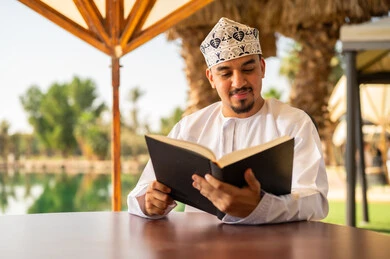 رجل عماني بالزي التقليدي يقرأ كتاباً في الخارج