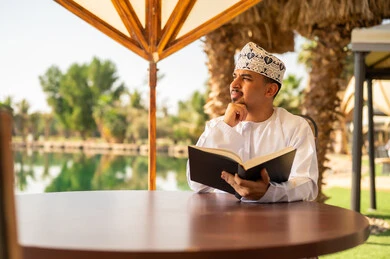 رجل عماني يقرأ كتاباً في الهواء الطلق أمام بحيرة
