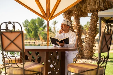 رجل عماني بالزي التقليدي يقرأ كتاباً في الهواء الطلق