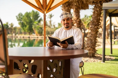 رجل عُماني بالزي التقليدي يقرأ على طاولة خارجية