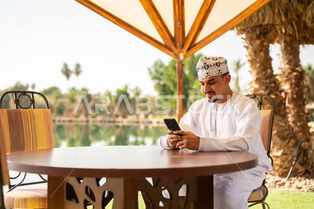رجل عماني يستخدم الهاتف الذكي في منتجع خارجي