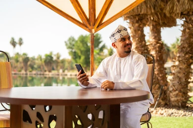 رجل عماني بالزي التقليدي مع هاتف ذكي في الخارج