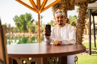 رجل عماني يحمل هاتف ذكي في منتجع خارجي