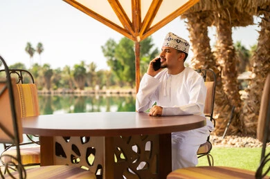 Omani Man in Traditional Dress Using Smartphone at Resort