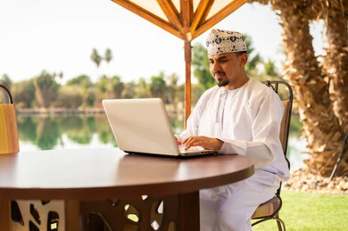 رجل عُماني يعمل على حاسوب محمول في الخارج