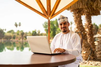 رجل عماني يستخدم الكمبيوتر المحمول في الهواء الطلق