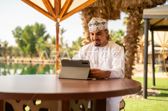 رجل عُماني يستخدم جهازاً لوحياً في منتجع خارجي