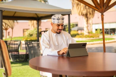 رجل عماني يستخدم جهاز لوحي في مقهى حديقة خارجي