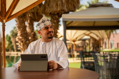 رجل عماني يستخدم جهاز لوحي في منتجع خارجي