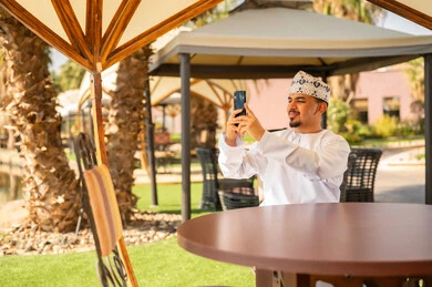 رجل عماني بالزي التقليدي يلتقط سيلفي في الحديقة